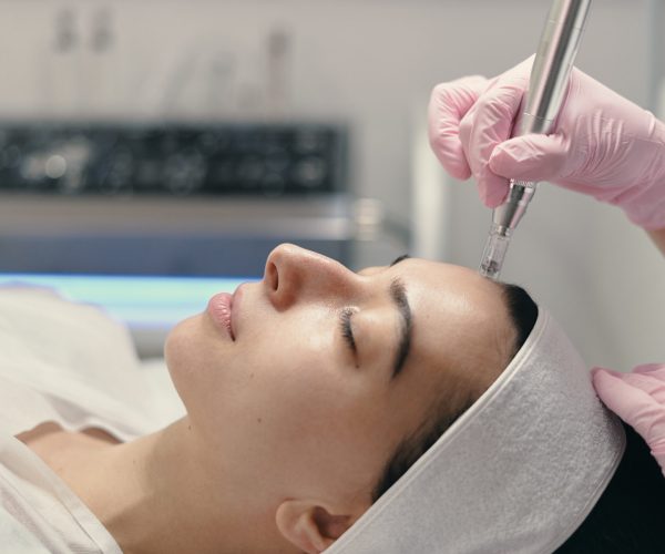 Model with closed eyes and hand's of doctor. Rejuvenating facial treatment. Model getting lifting therapy massage in a beauty SPA salon. Cosmetological clinic, procedure.